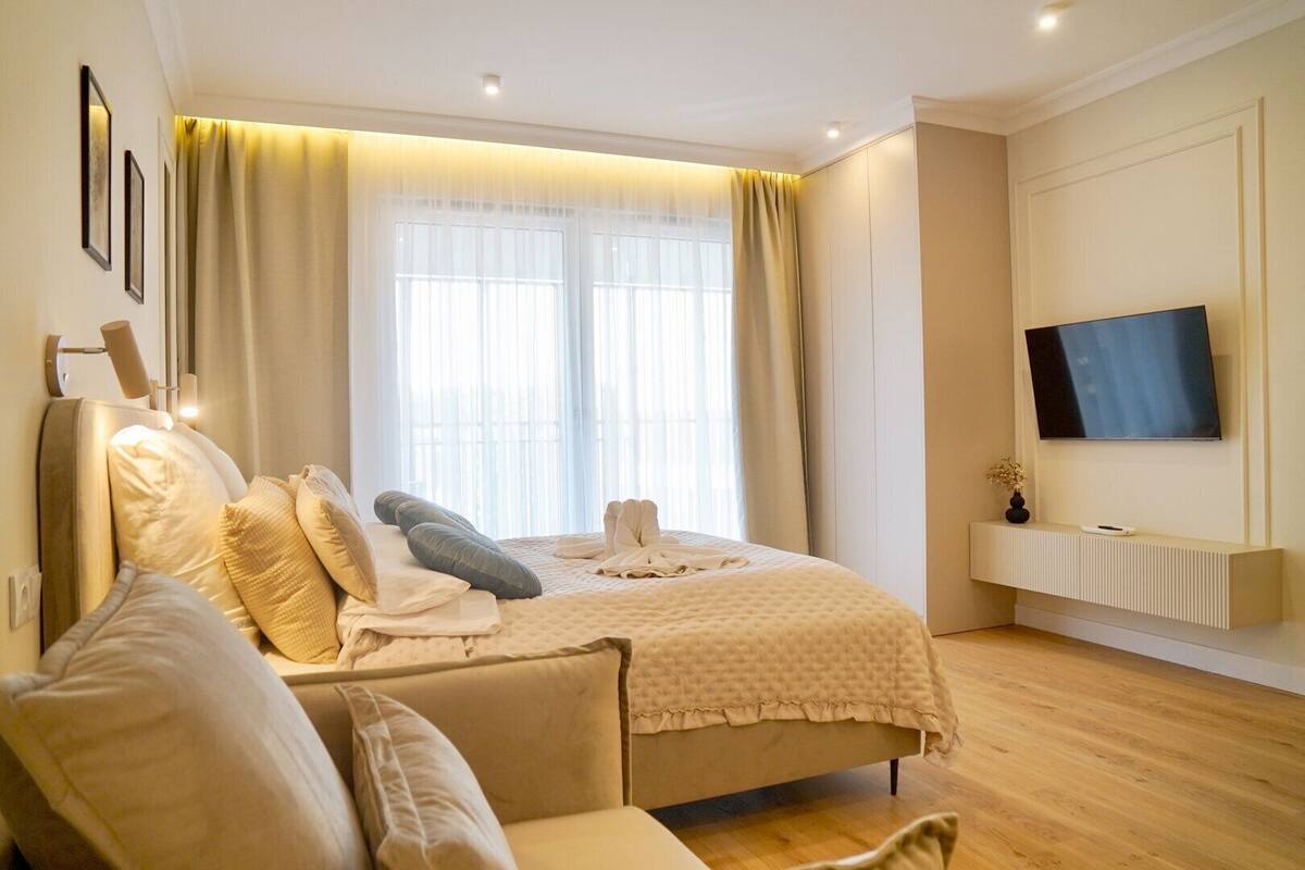 A modern bedroom with a large bed, a TV mounted on the wall, and a bedside table with a vase.