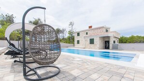 A pool area with a swing chair, a modern house, and a stone-tiled deck. - Villa Sana, on the beach with swimming pool (Vir)