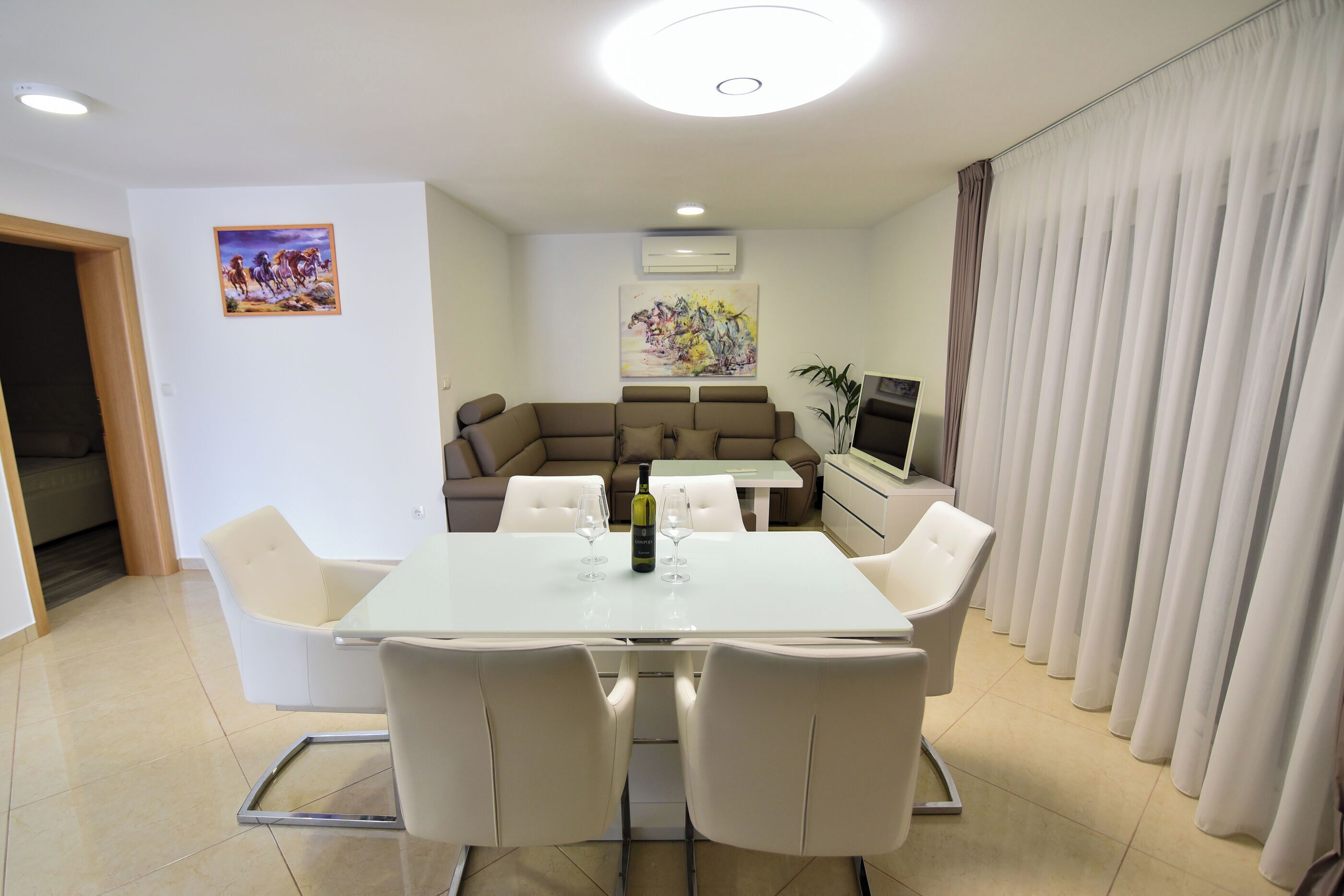 Un espace repas moderne avec une table et des chaises blanches, un canapé et un téléviseur.
