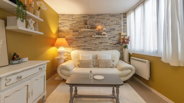 Ein gemütliches Wohnzimmer mit Steinwand, einem weißen Sofa, einem Couchtisch und einer Lampe.