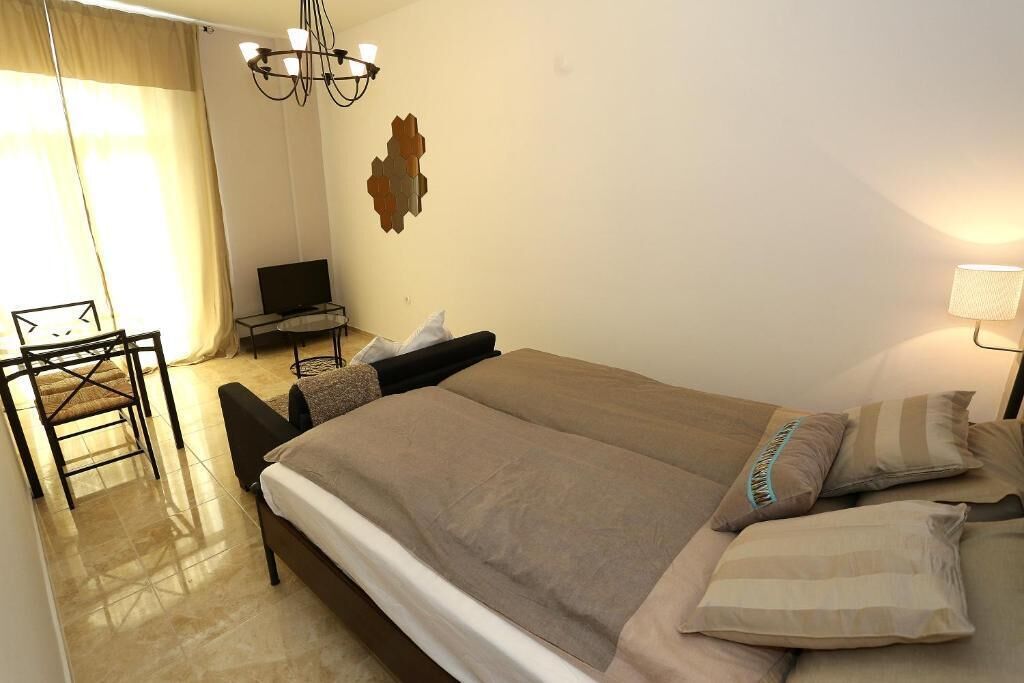 A bedroom with a bed, a chair, a desk with a computer, and a wall-mounted light fixture.