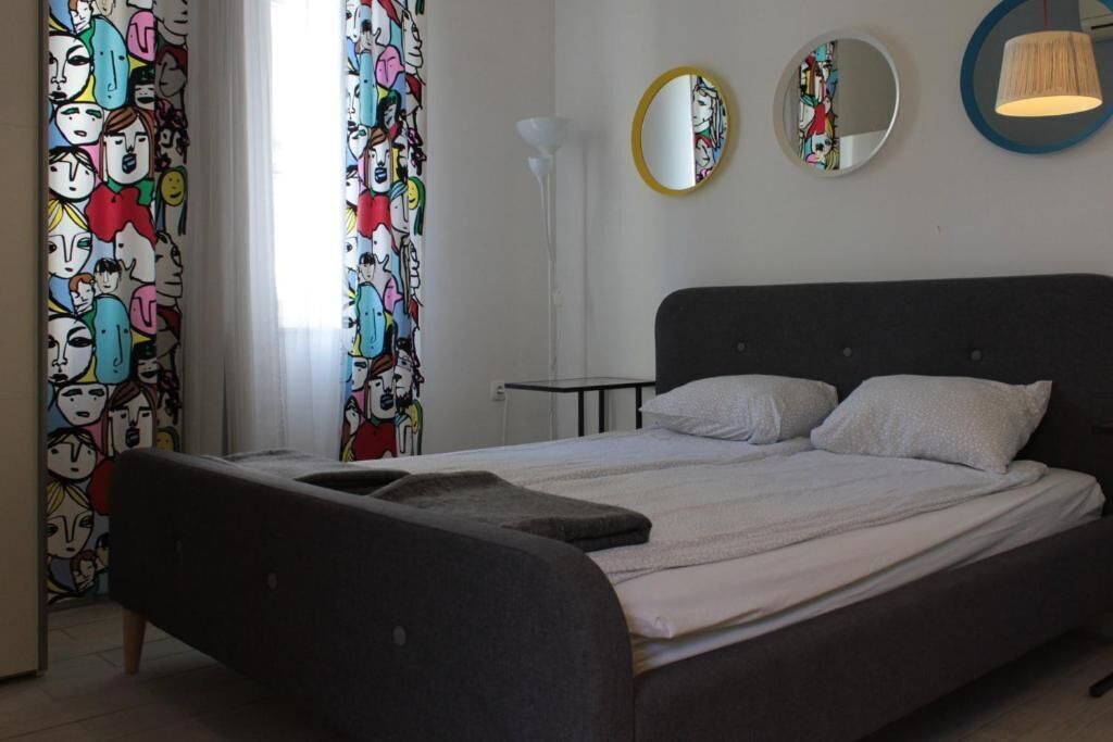A bedroom with a bed, a bedside table, a lamp, and a mirror on the wall.