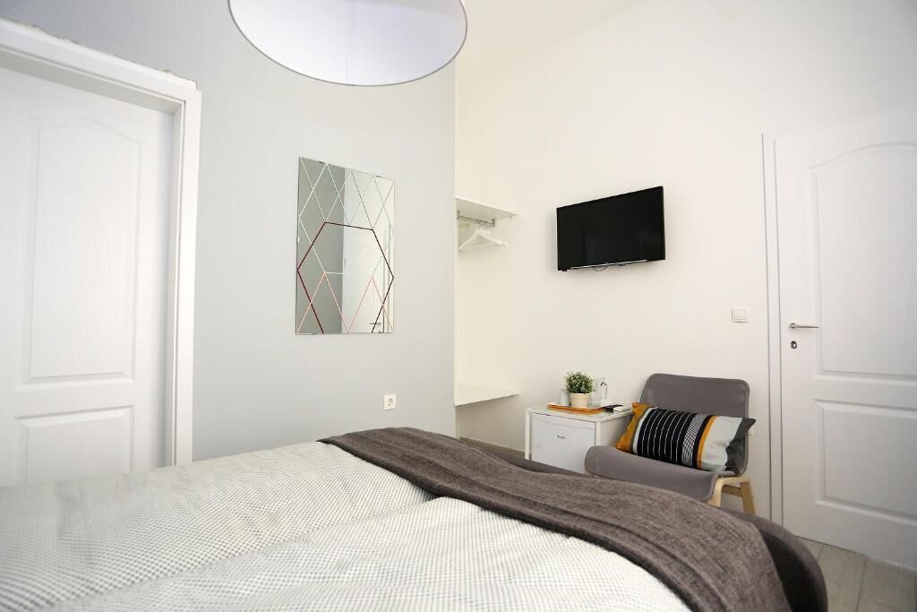 Une chambre à coucher moderne avec un lit, un téléviseur fixé au mur et un petit bureau avec une chaise.