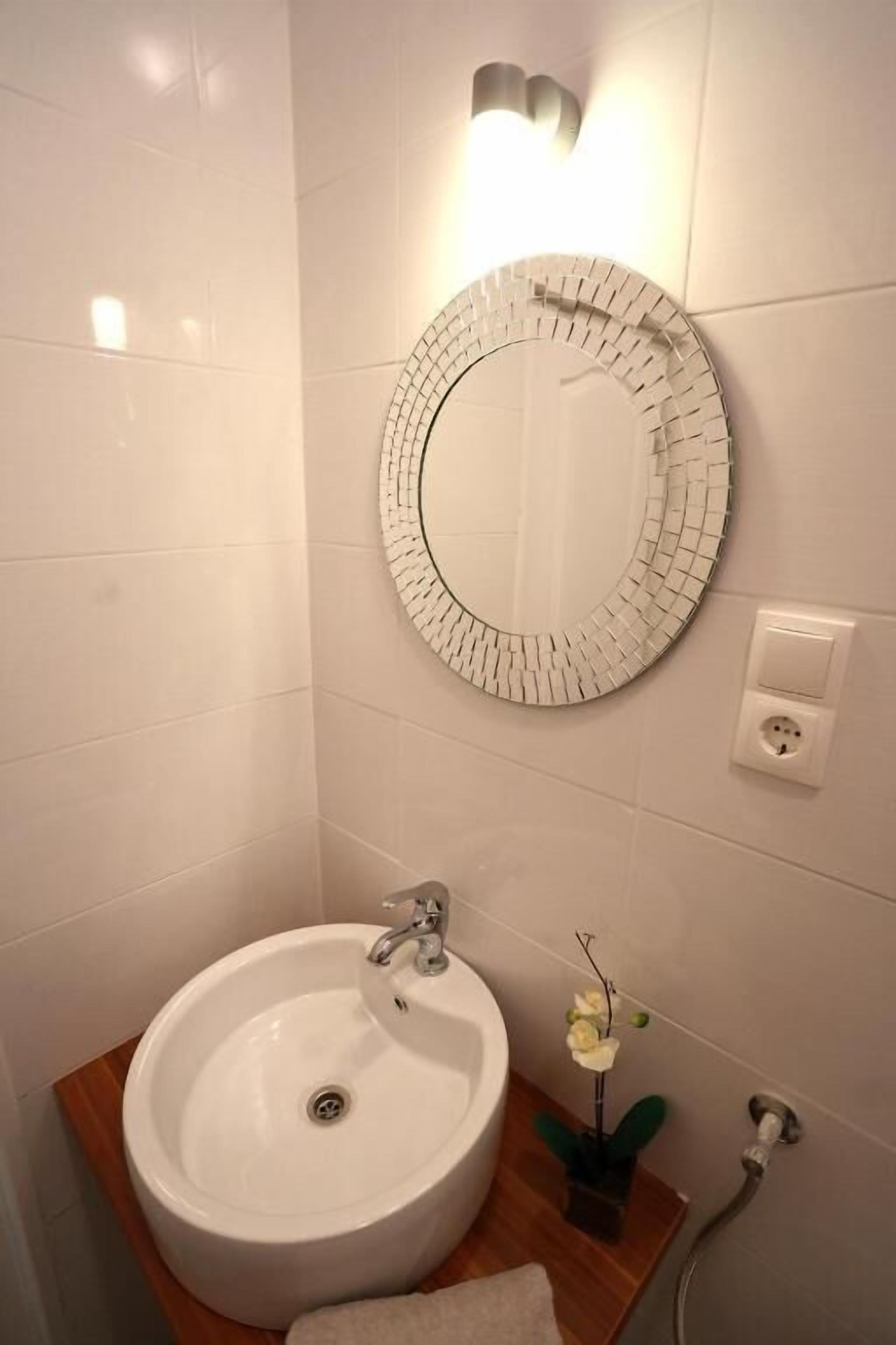 A bathroom with a white sink, a round mirror with a brick pattern, and a small potted plant.