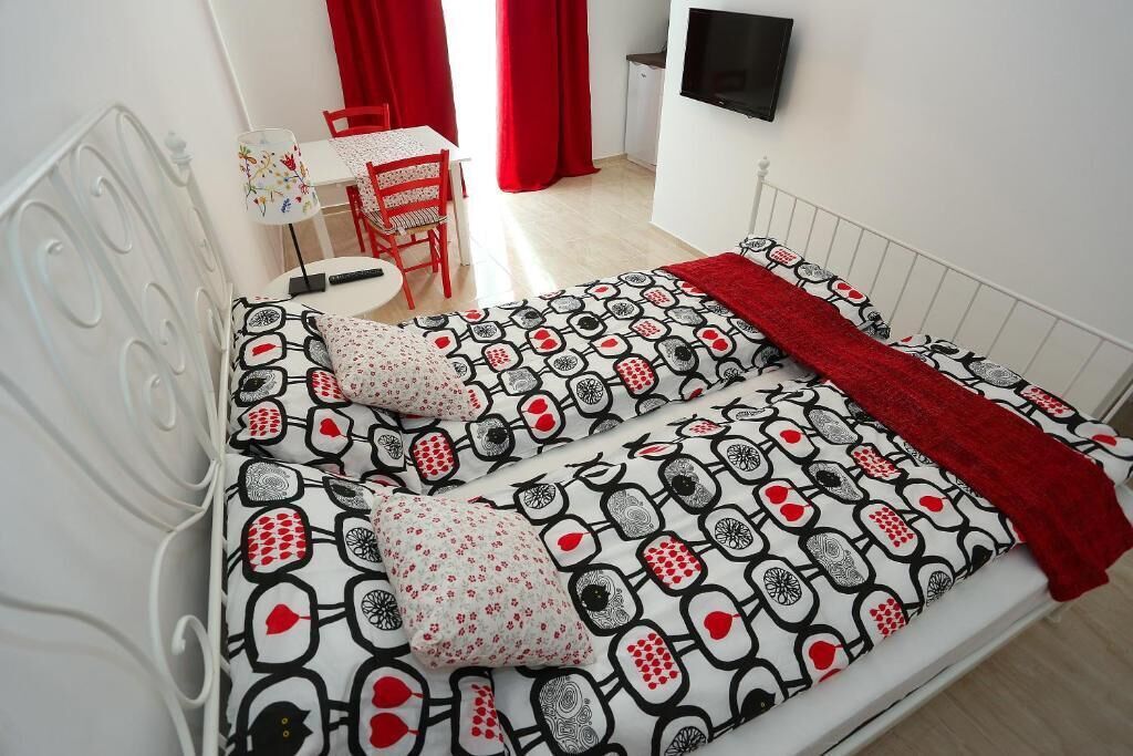 A bedroom with a patterned bedspread, a red blanket, and a white headboard.