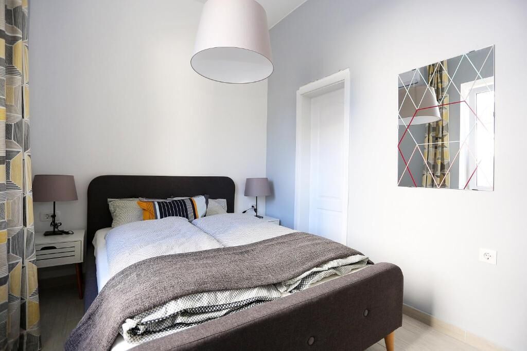 A bedroom with a bed, bedside tables, a lamp, a mirror, and a geometric wall art piece.