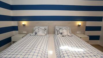 A room with two beds, each with a patterned bedspread and matching pillows, against a wall with blue and white stripes.