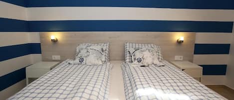 A room with two beds, each with a patterned bedspread and matching pillows, against a wall with blue and white stripes.