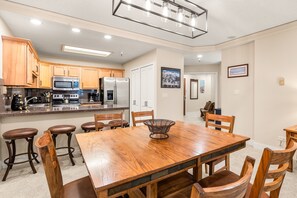 A modern kitchen with wooden cabinets, stainless steel appliances, and a large dining table with bar stools.