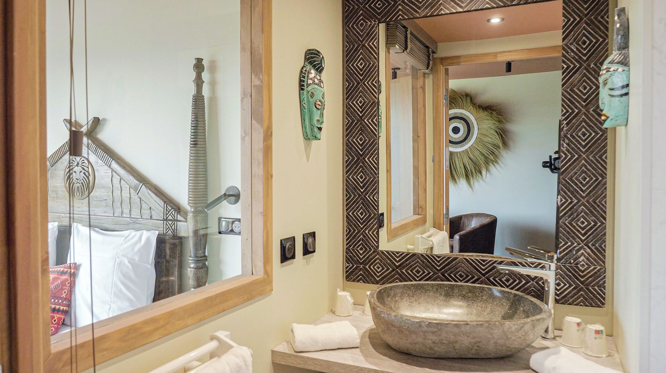 A bathroom with a large mirror, a stone basin, and a patterned wall.