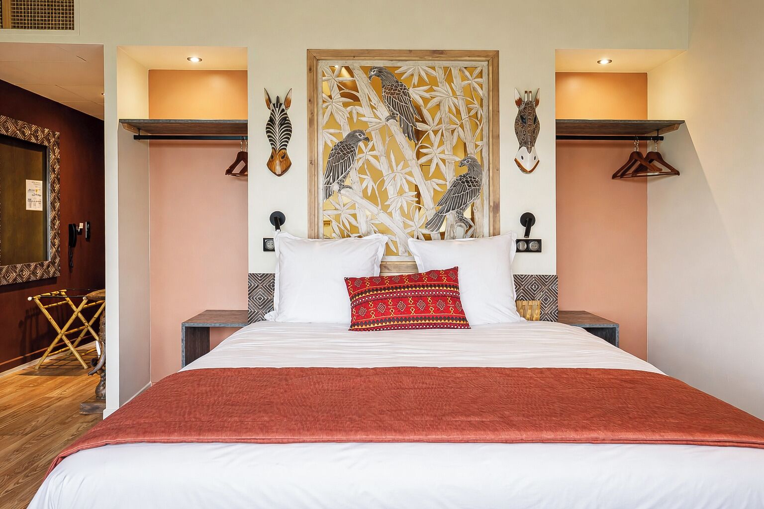 Una habitación de hotel con una cama grande, un cabecero decorativo, obras de arte en la pared y suelo de madera.