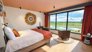 A modern hotel room with a large bed, a view of a green landscape, a round decorative wall piece, and a small table with a kettle. - Le royaume des Lions  (Lumigny-Nesles-Ormeaux)