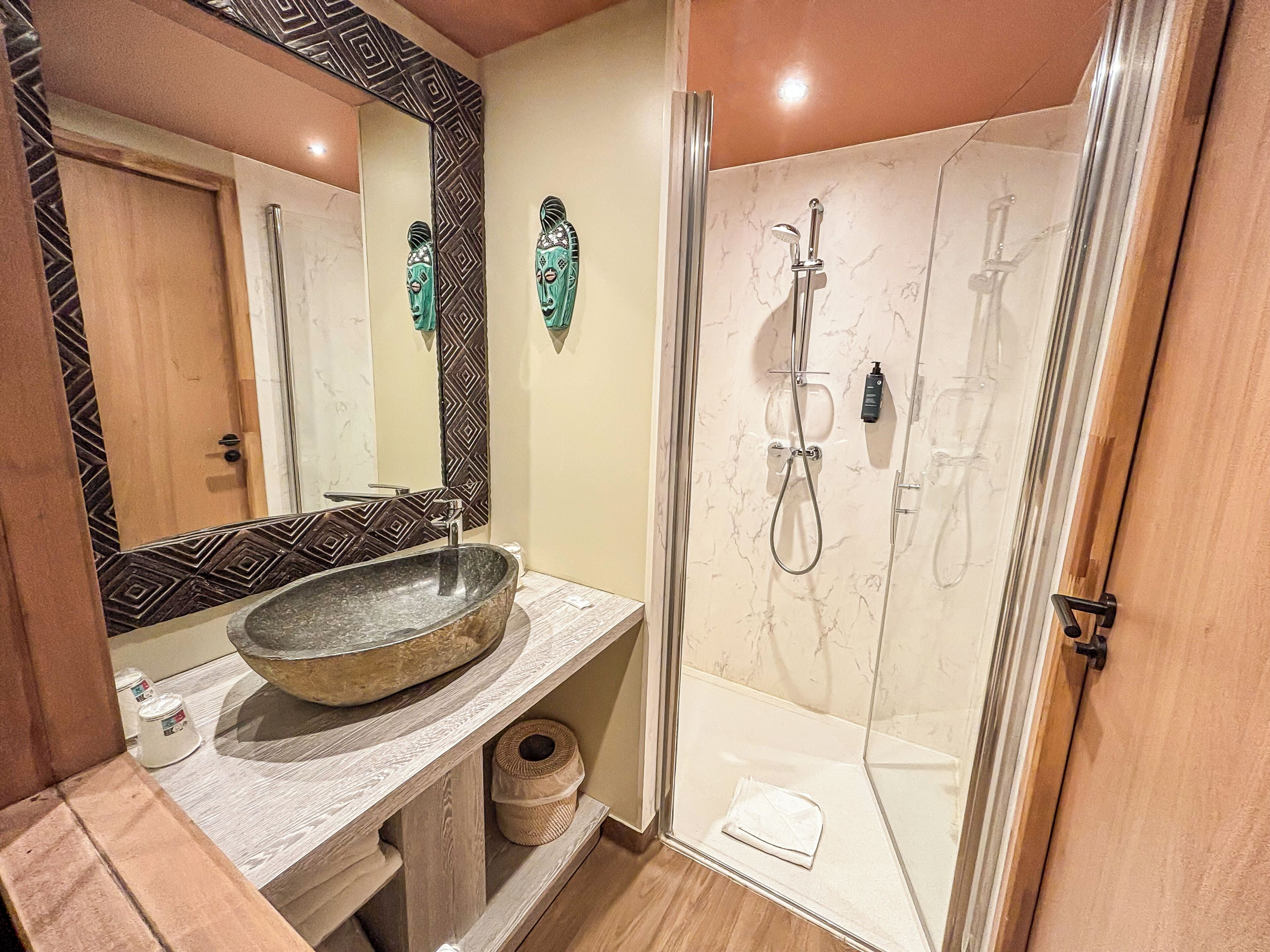 Un baño con un lavamanos ovalado grande, ducha con cabezal de ducha de mano y espejo con diseño geométrico.