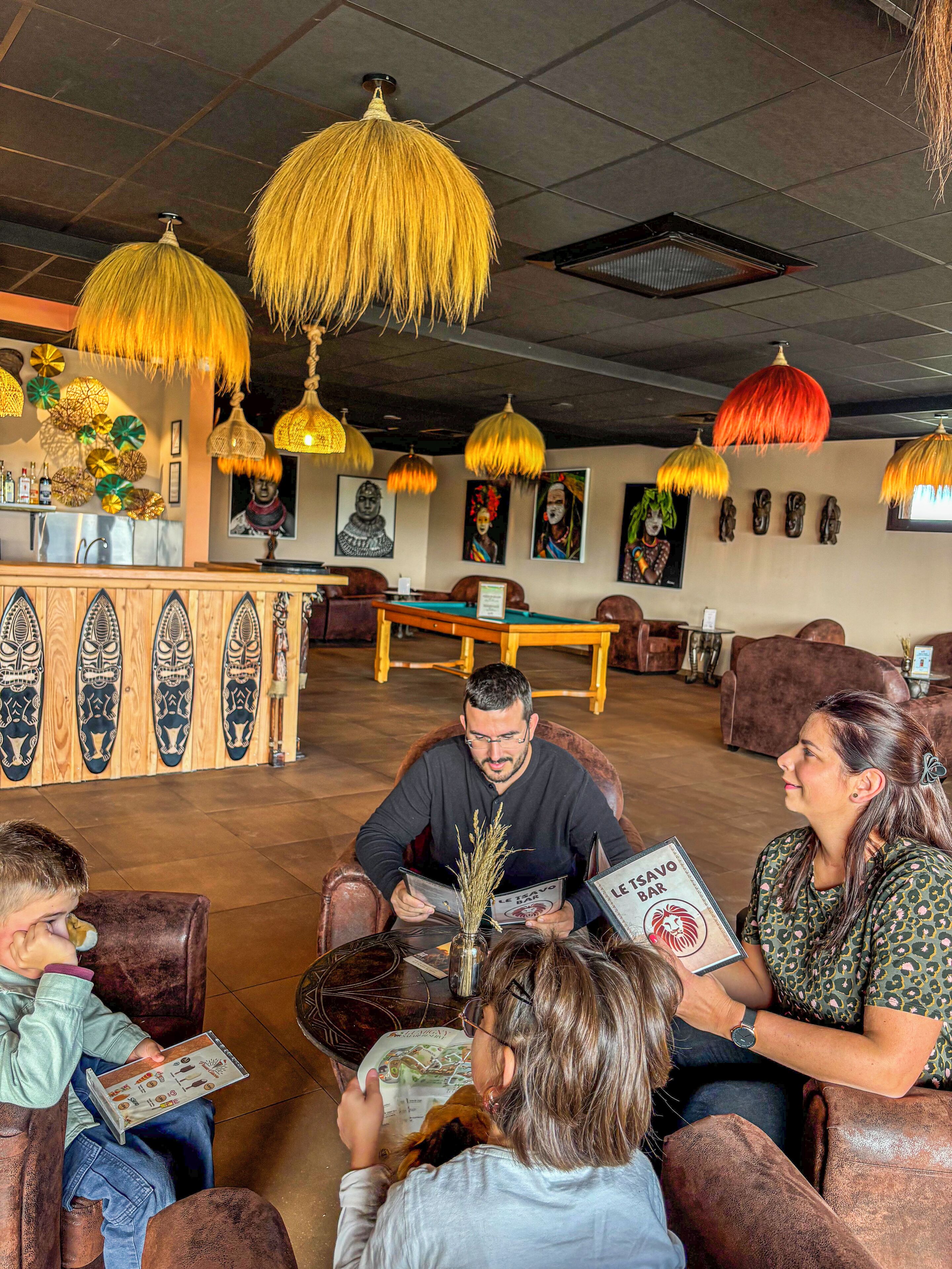 Un grupo de personas sentadas en una sala con zona de bar, mobiliario de madera y lámparas colgantes.