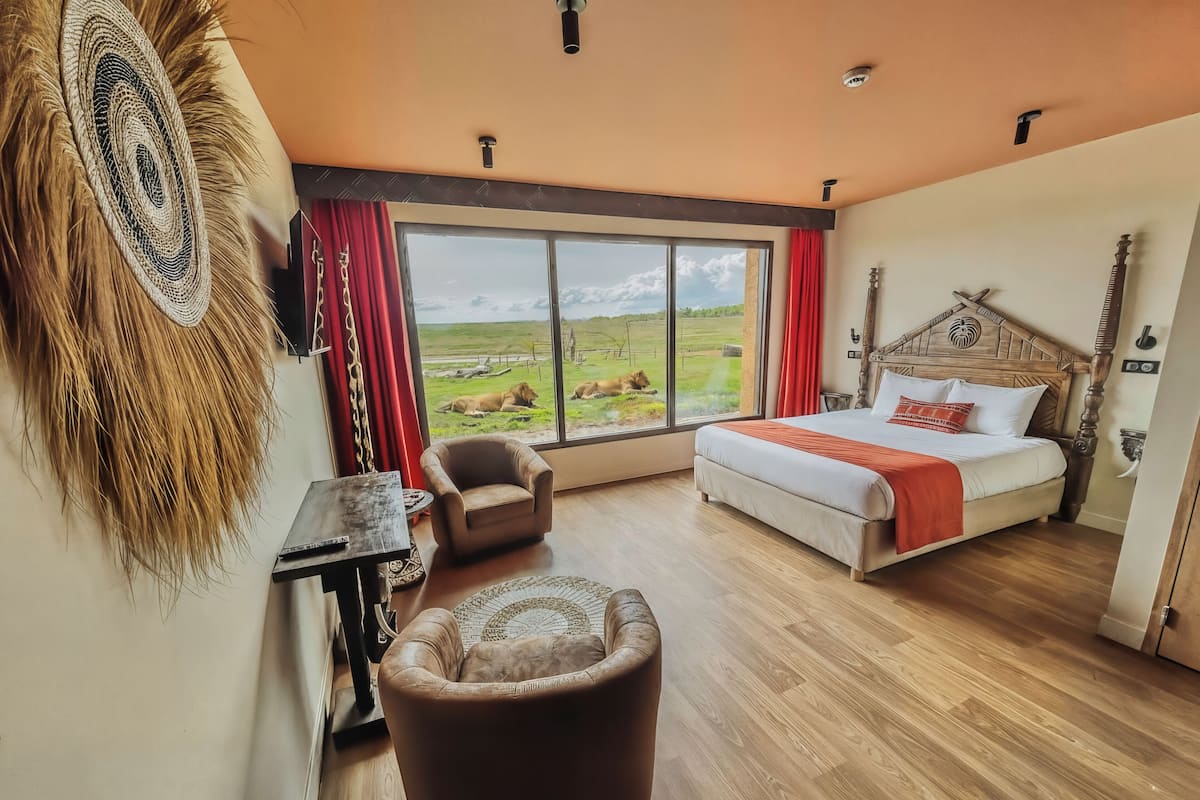 A bedroom with a large window, a bed, a chair, and a small table.