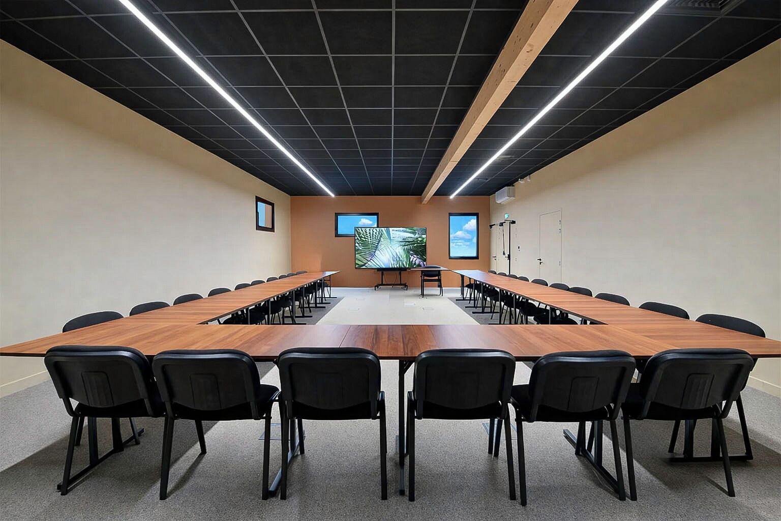 Un salón de conferencias con una larga mesa, sillas, una pantalla de proyector y un ventanal grande.