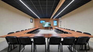 Un salón de conferencias con una larga mesa, sillas, una pantalla de proyector y un ventanal grande.