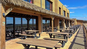An outdoor patio area with wooden picnic tables and a thatched roof structure. - Le royaume des Lions  (Lumigny-Nesles-Ormeaux)