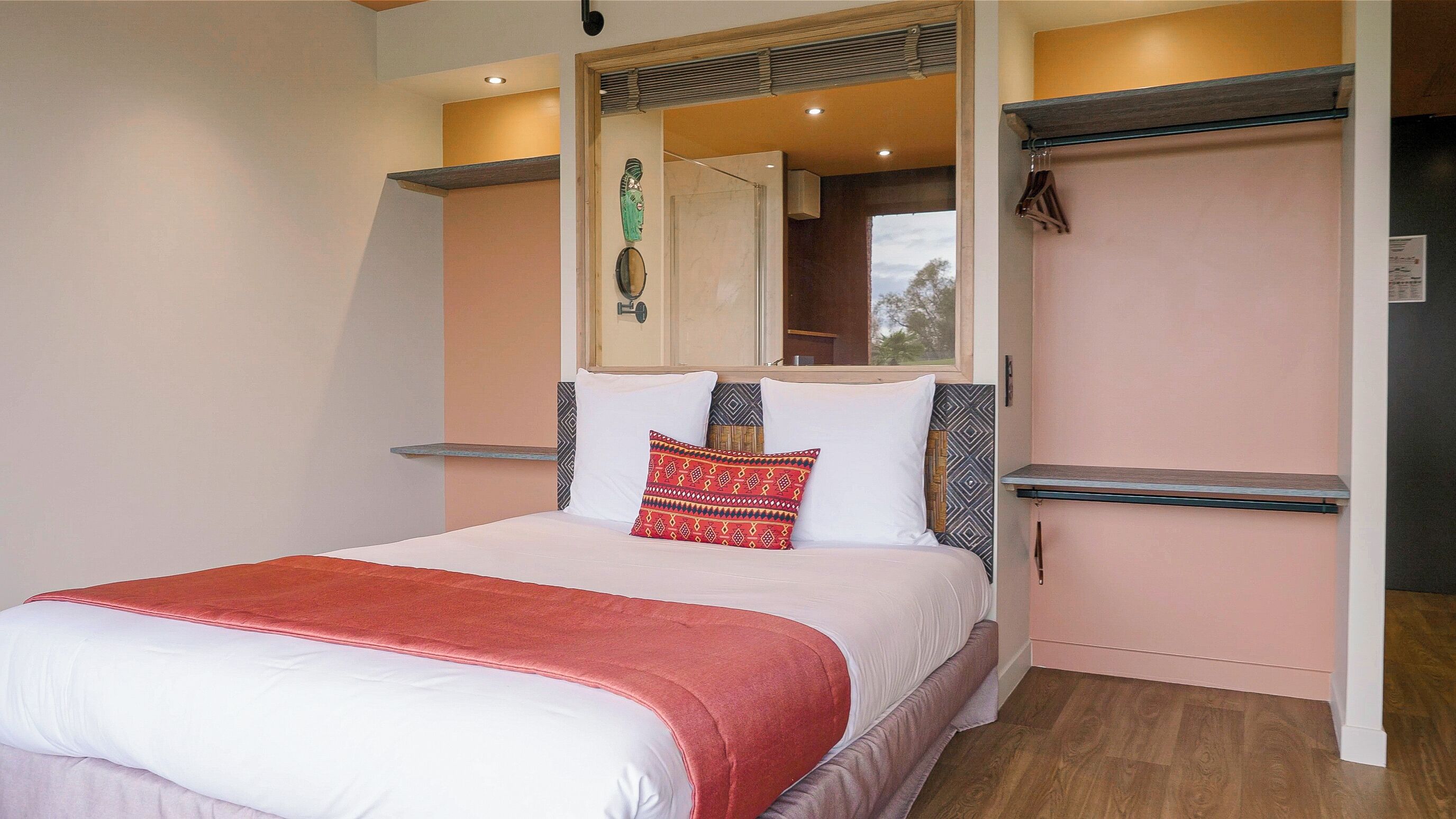 A neatly made bed with a red blanket, a bedside table, and a mirror above it.