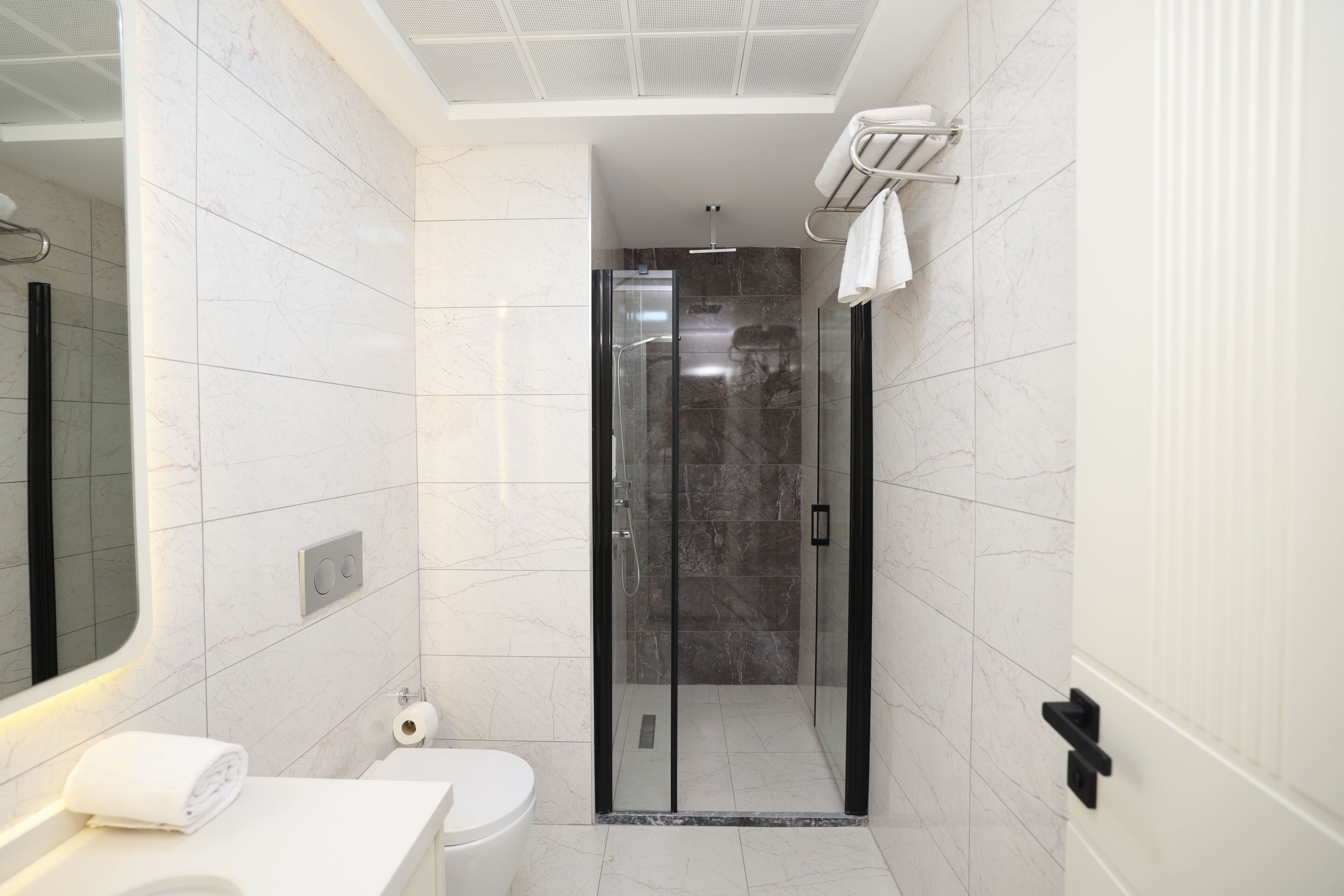 Un baño moderno con ducha de vidrio, inodoro y lavamanos con barra para toallas.