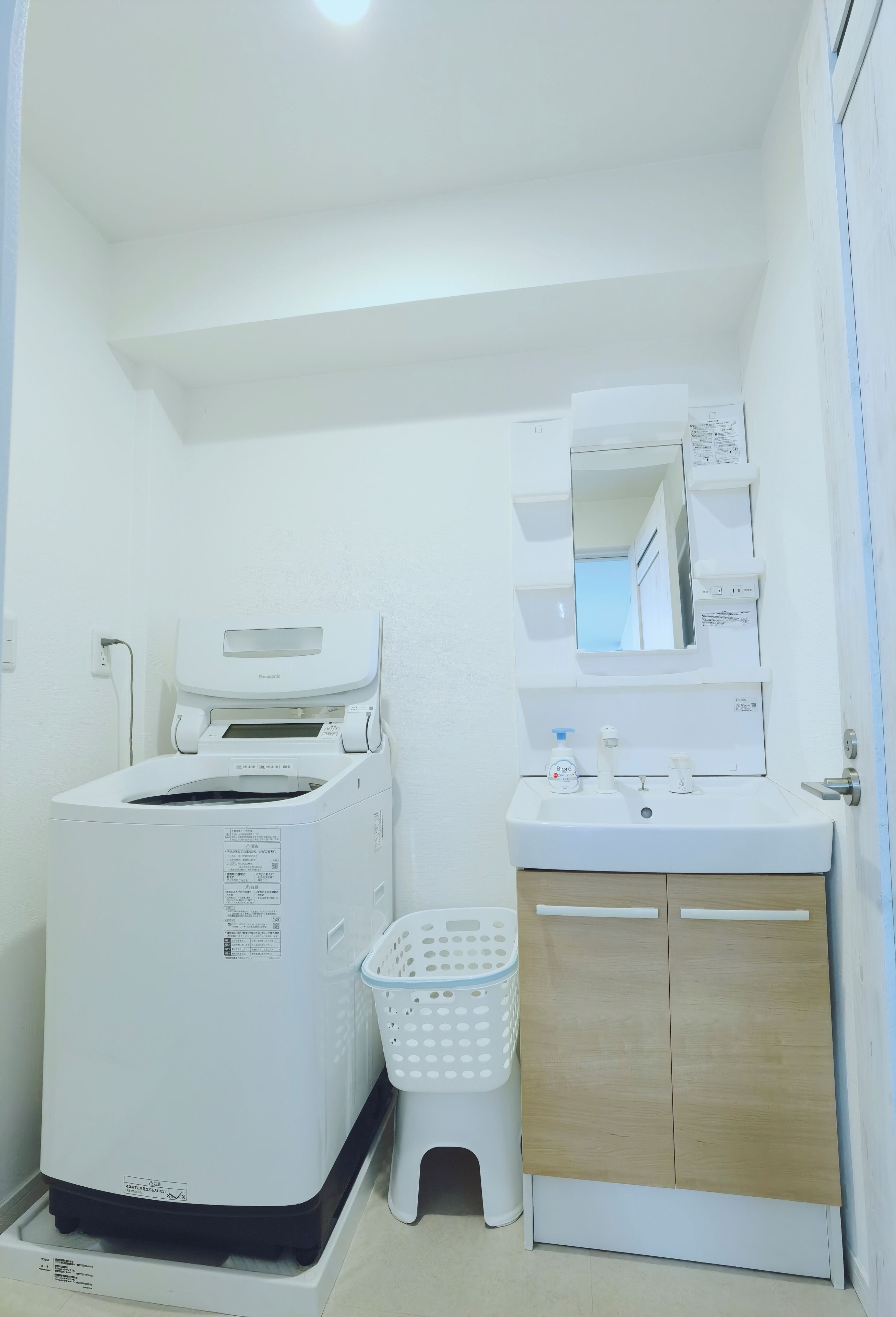 A compact laundry room with a washing machine, a sink, a mirror, and a wooden cabinet.