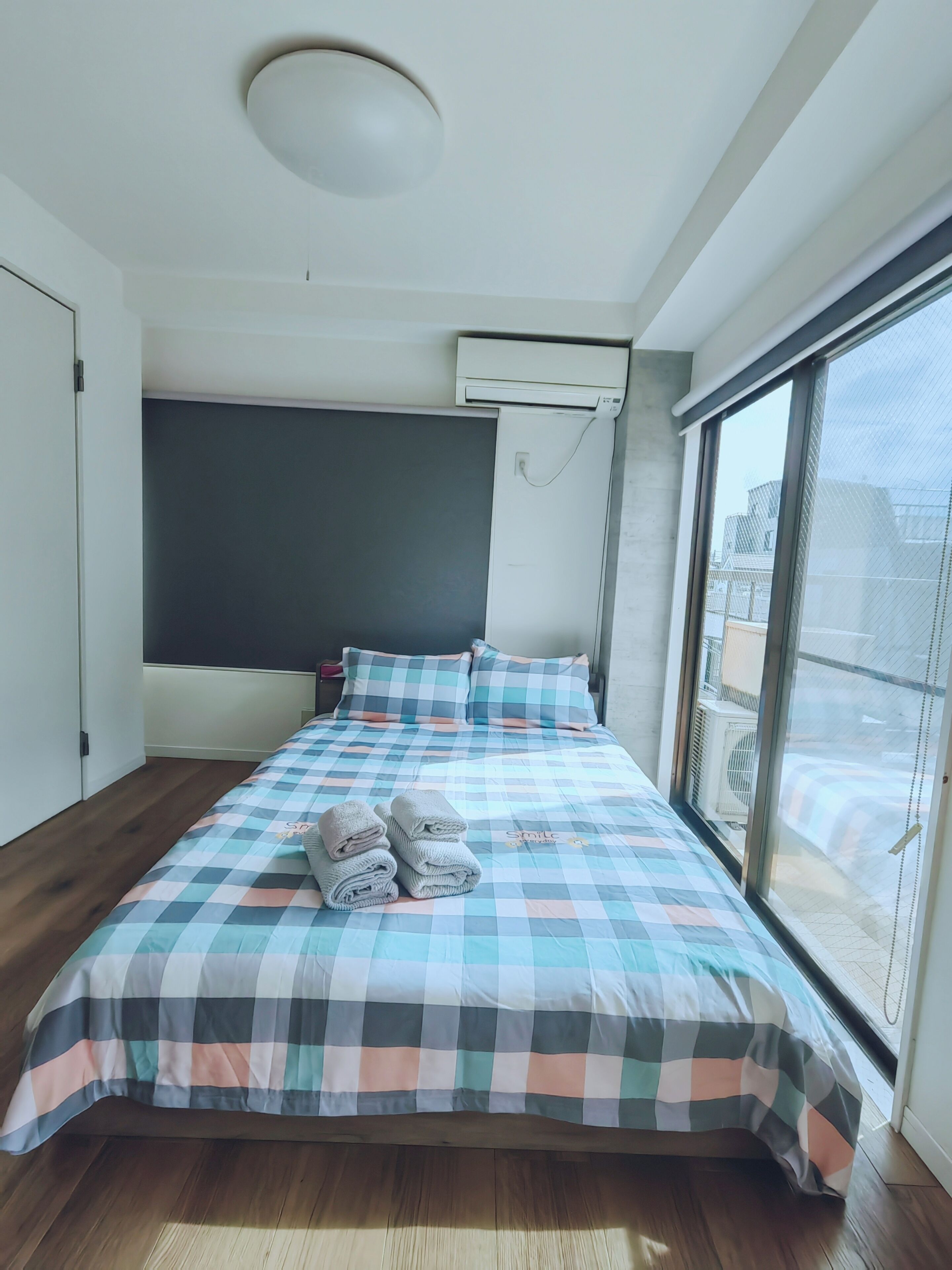 A modern bedroom with a large bed, a ceiling light, an air conditioning unit, and a large window.