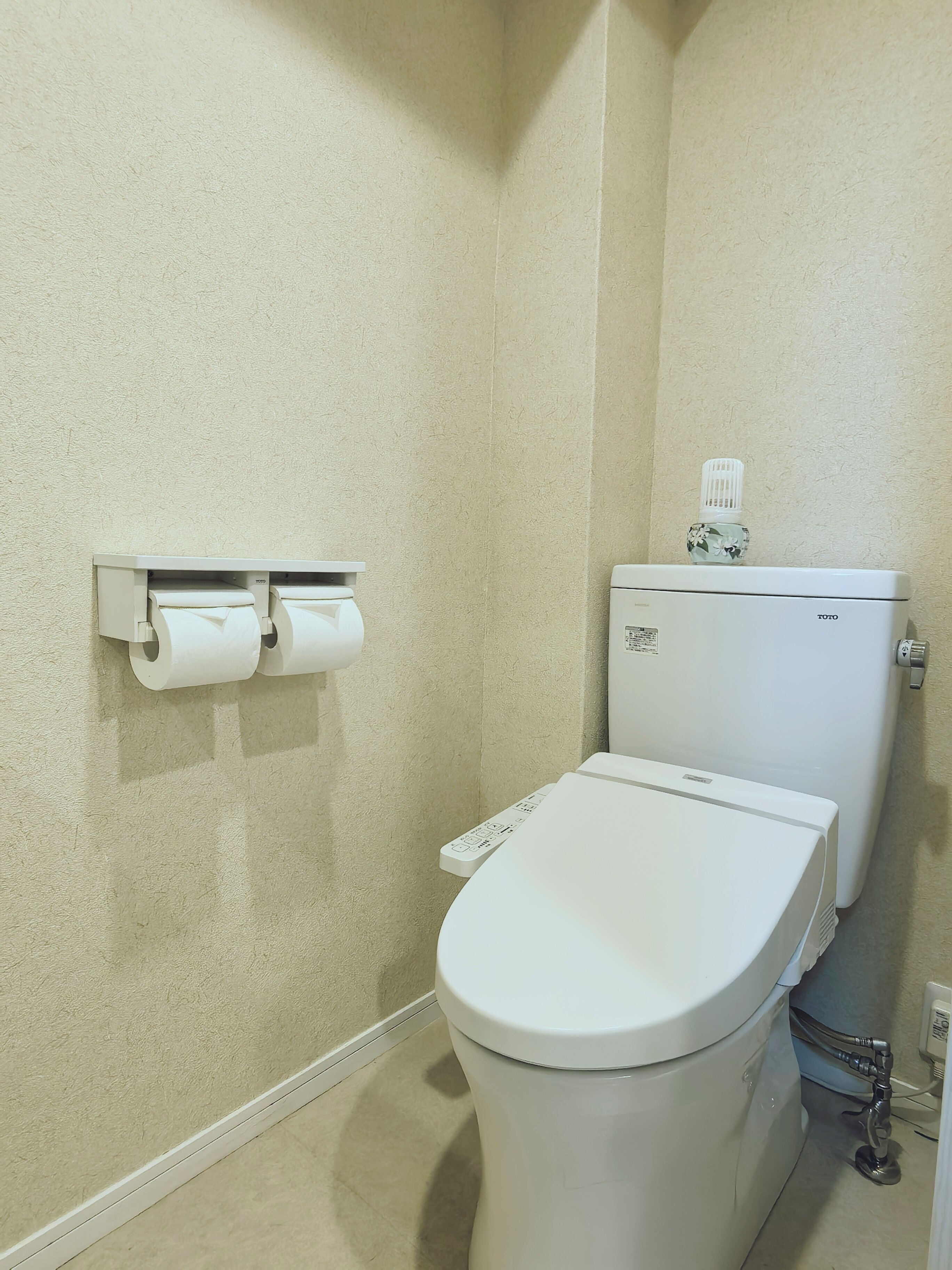 A bathroom with a toilet, a toilet paper holder, and a water bottle on the wall.
