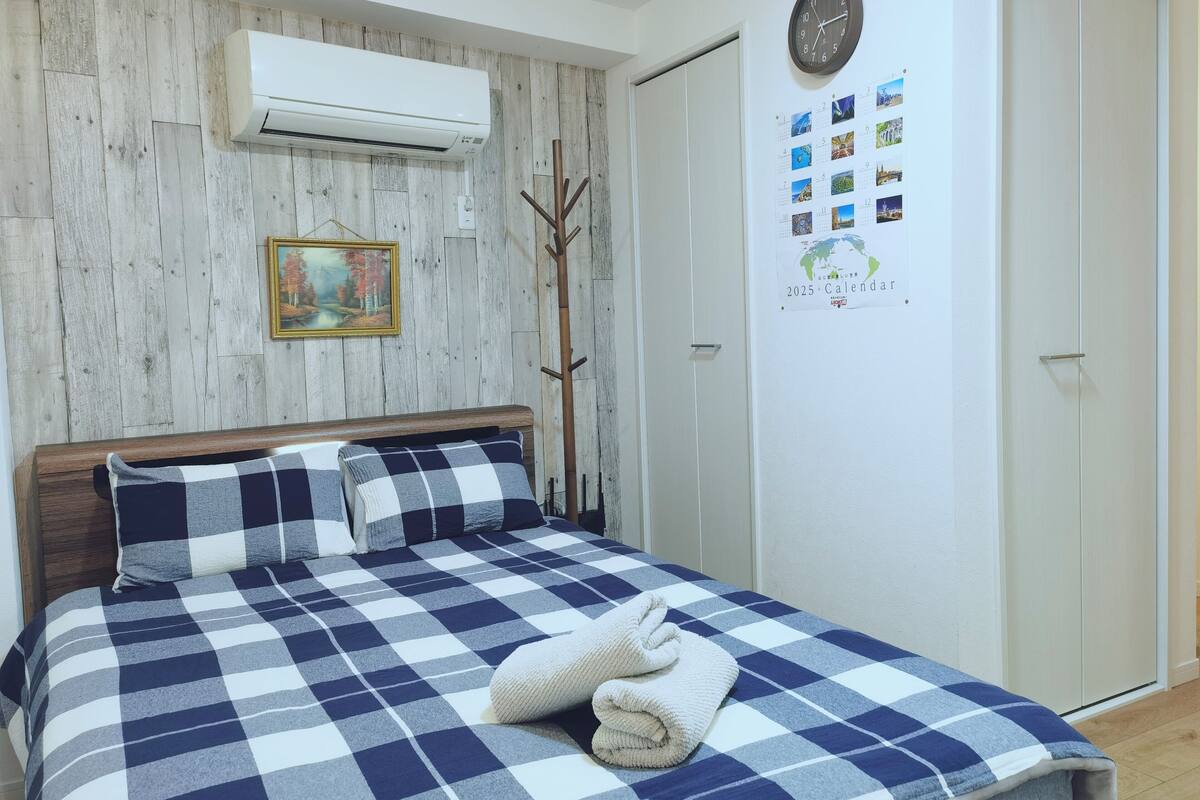 Une chambre à coucher comprenant un lit, un climatiseur fixé au mur, un porte-manteau en bois, un calendrier et une armoire.