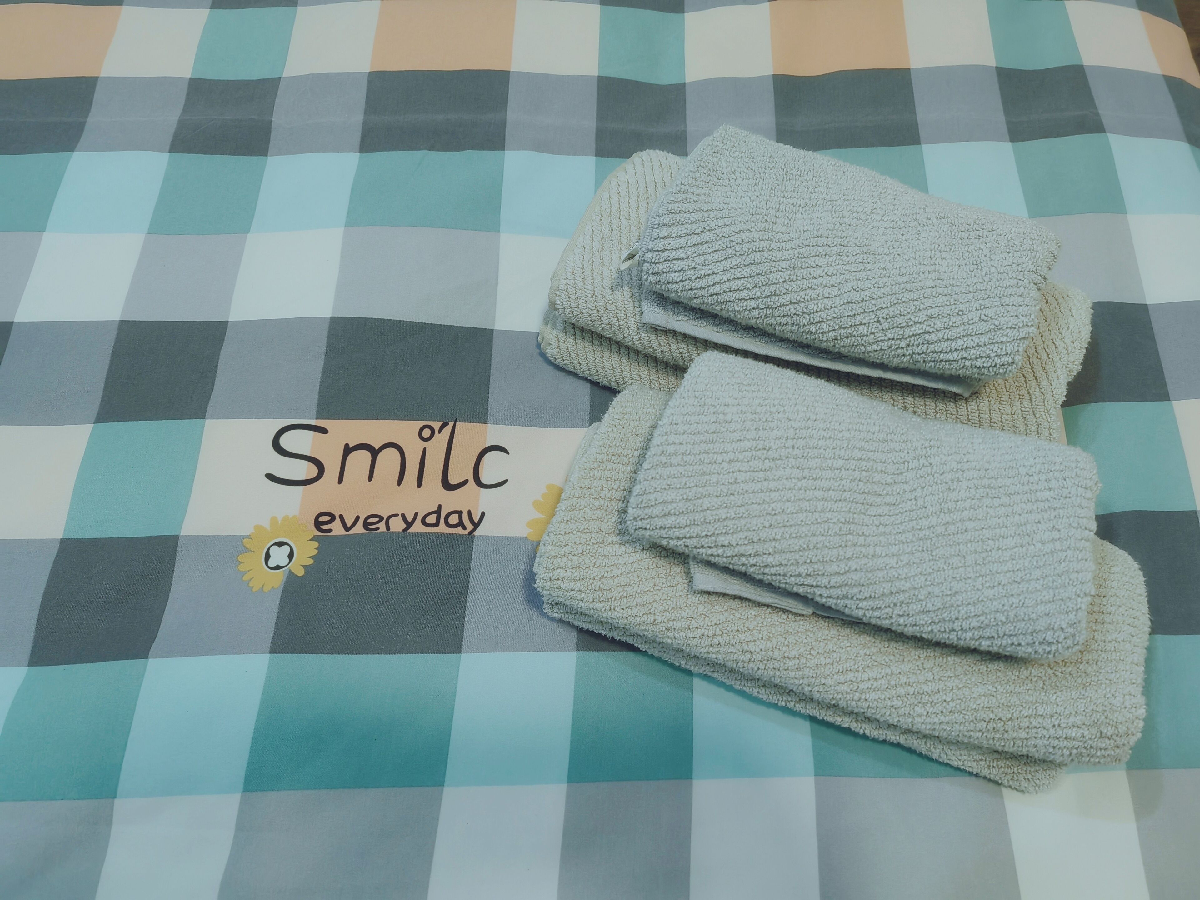 A checkered bedspread with a folded towel and a sign that reads "Smile everyday" with a sun and flower icon.