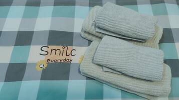 A checkered bedspread with a folded towel and a sign that reads "Smile everyday" with a sun and flower icon.