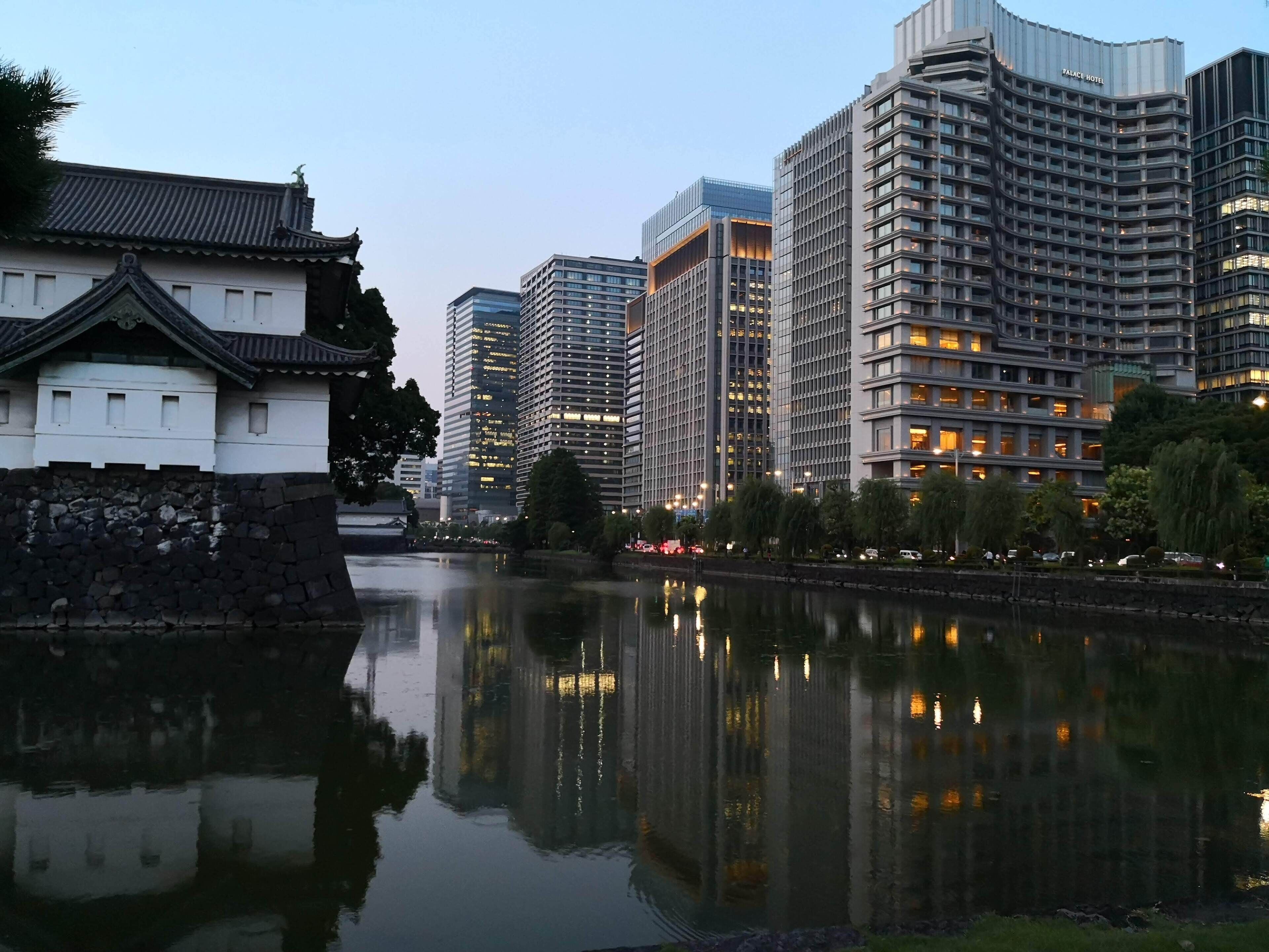 A modern cityscape with a traditional building reflecting in a calm river.