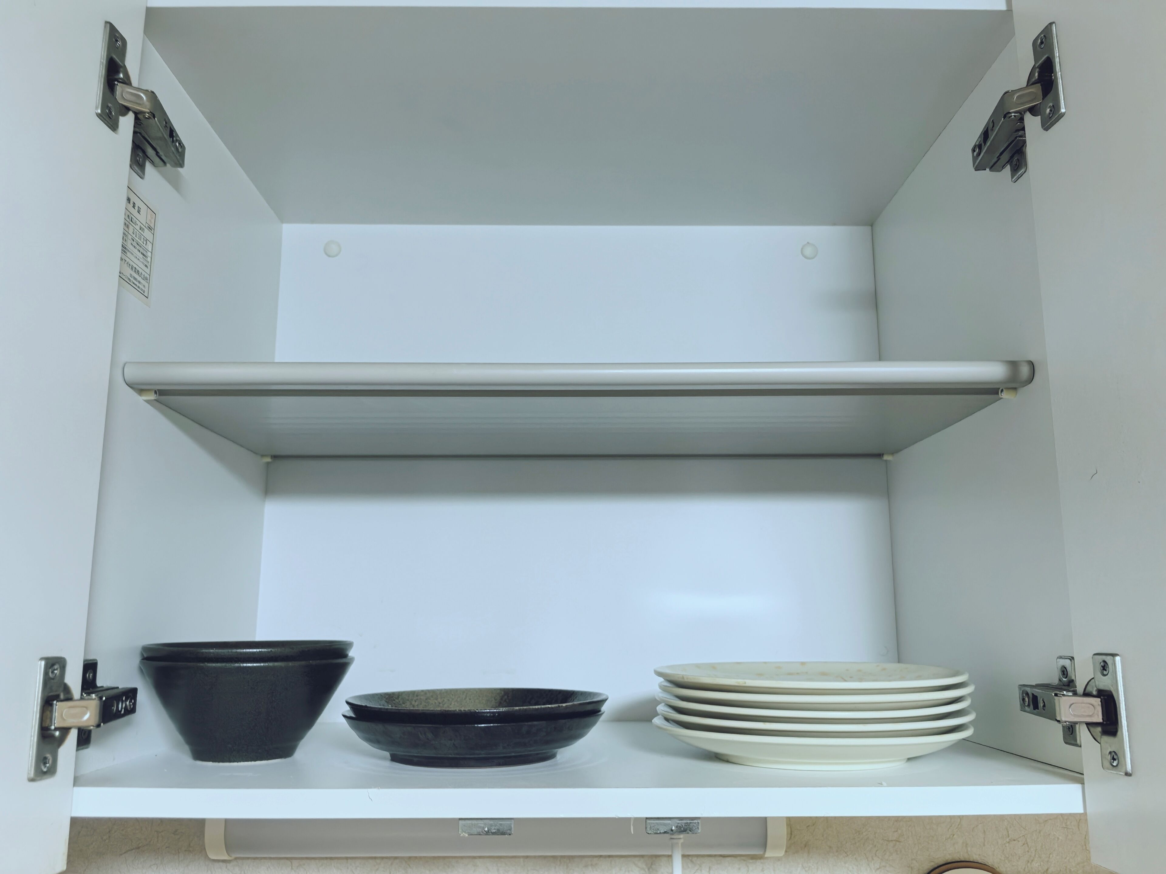 Un meuble blanc à deux étagères, l’une contenant des bols noirs et l’autre, des assiettes blanches.