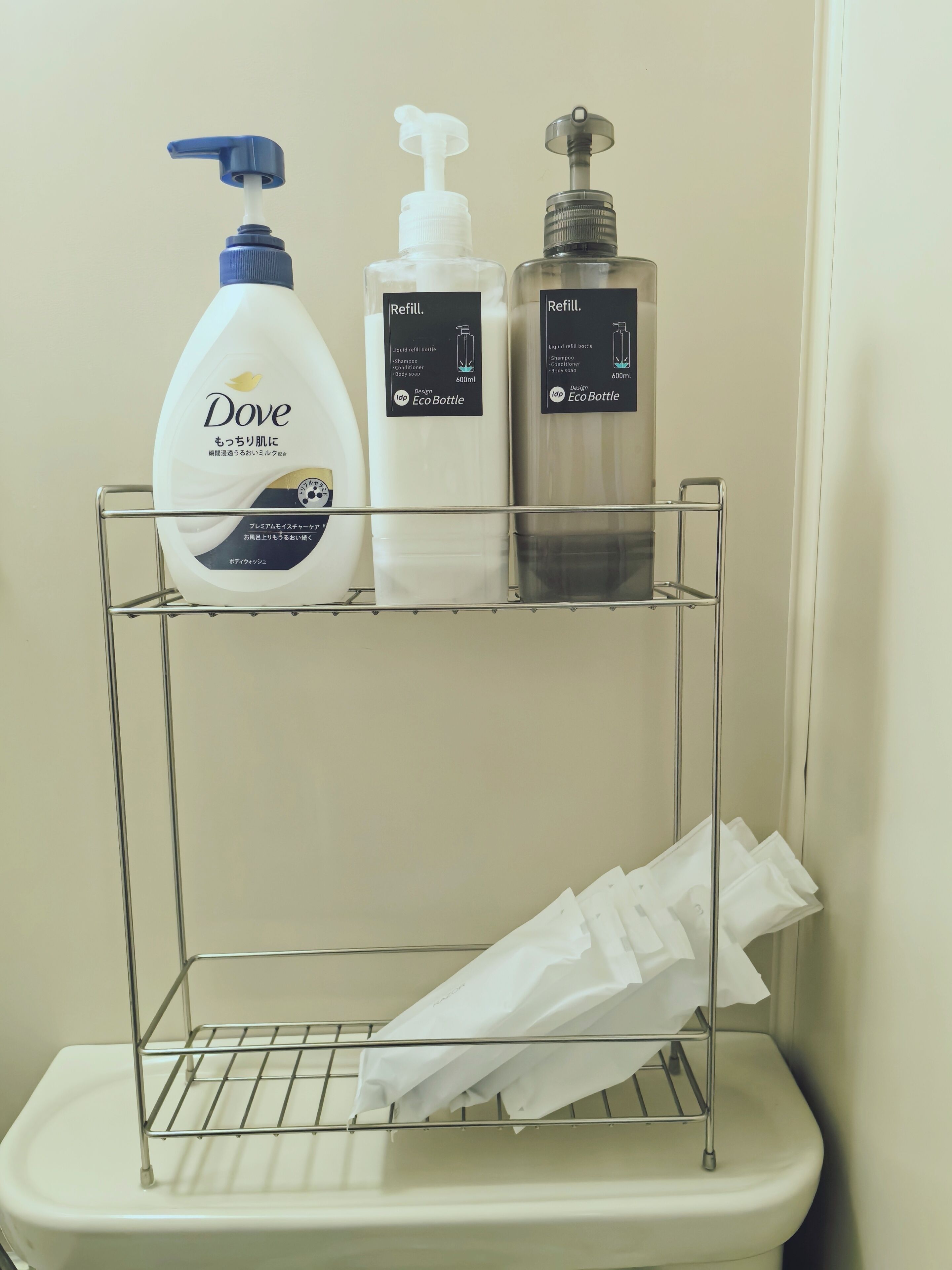 Casa de banho com uma prateleira de metal com garrafas de champô e gel de banho Dove, um porta-lenços e uma sanita.