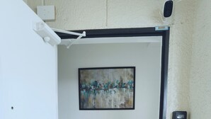 Ein schmaler Flur mit einer zur Zimmer führenden Tür, einem Gemälde an der Wand und einem Sicherheitstastenfeld auf der rechten Seite.