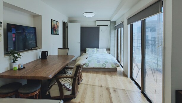 Ein modernes Hotelzimmer mit einem Holztisch, einem Bett mit gemusterten Betttextilien, einem großen Fenster mit Blick und einem an der Wand befestigten Flachbildfernseher.