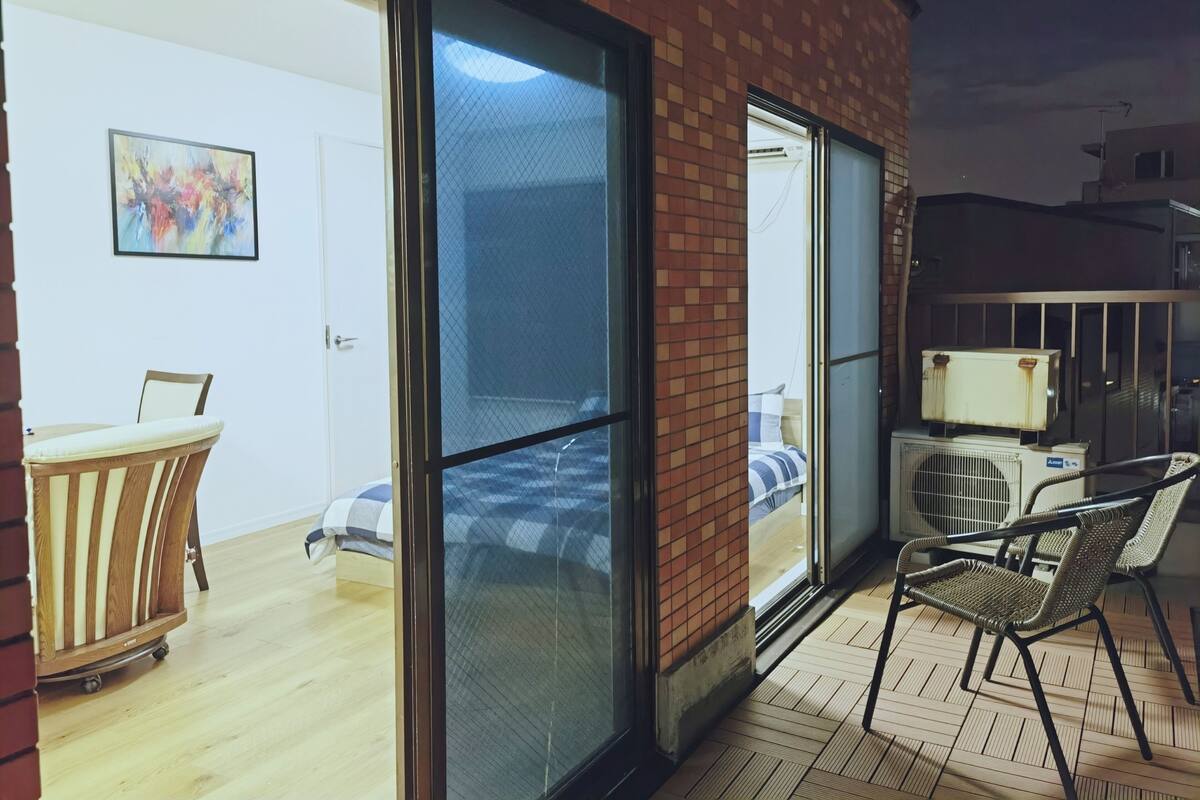 Une chambre dotée d’une porte-fenêtre coulissante donnant sur un balcon, d’un lit avec un oreiller à rayures, d’une chaise et d’un appareil de climatisation.
