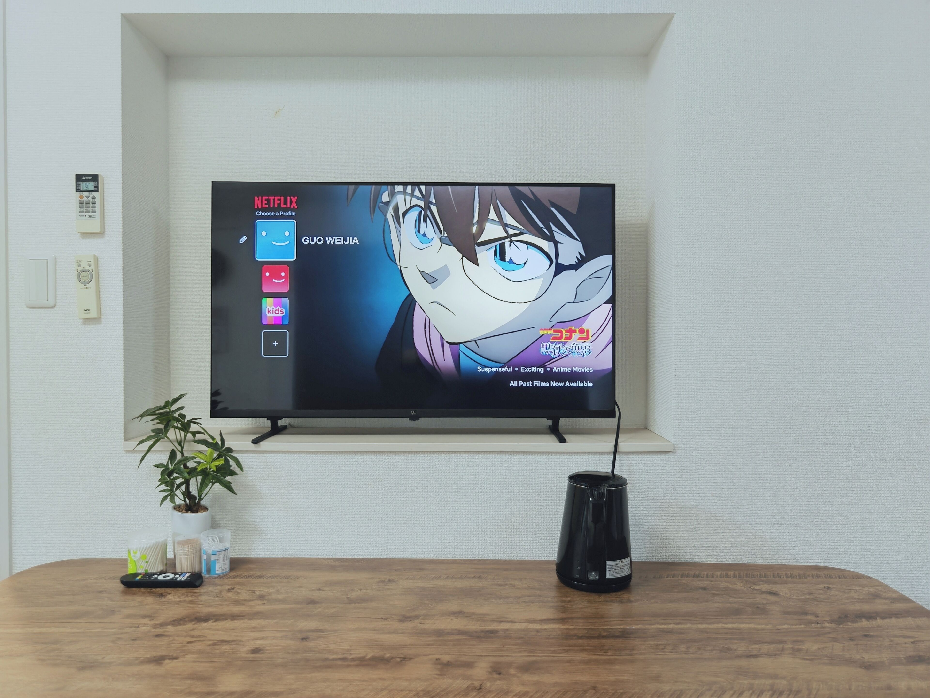 Un téléviseur fixé au mur affiche un écran de sélection de profils avec du contenu d’animation japonaise (anime).
