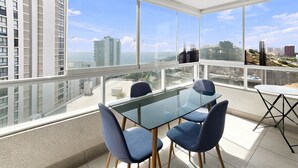 Una habitación moderna con una mesa y sillas de vidrio, ventanas amplias con vista a la ciudad y un balcón.