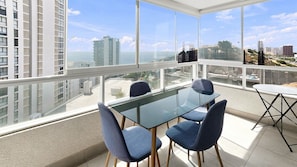 A modern room with a glass table and chairs, large windows with a city view, and a balcony.