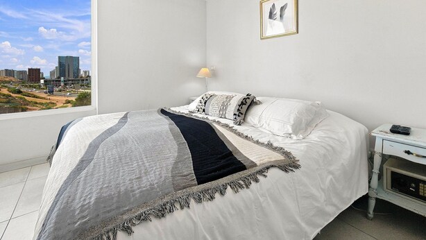 Un dormitorio con cama, mesita de noche, lámpara y vistas a la ciudad.