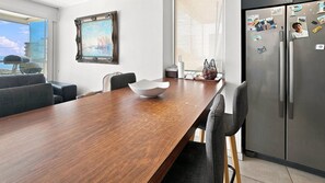 Une cuisine moderne avec une table à manger en bois, des chaises, un réfrigérateur et une fenêtre donnant sur la ville.