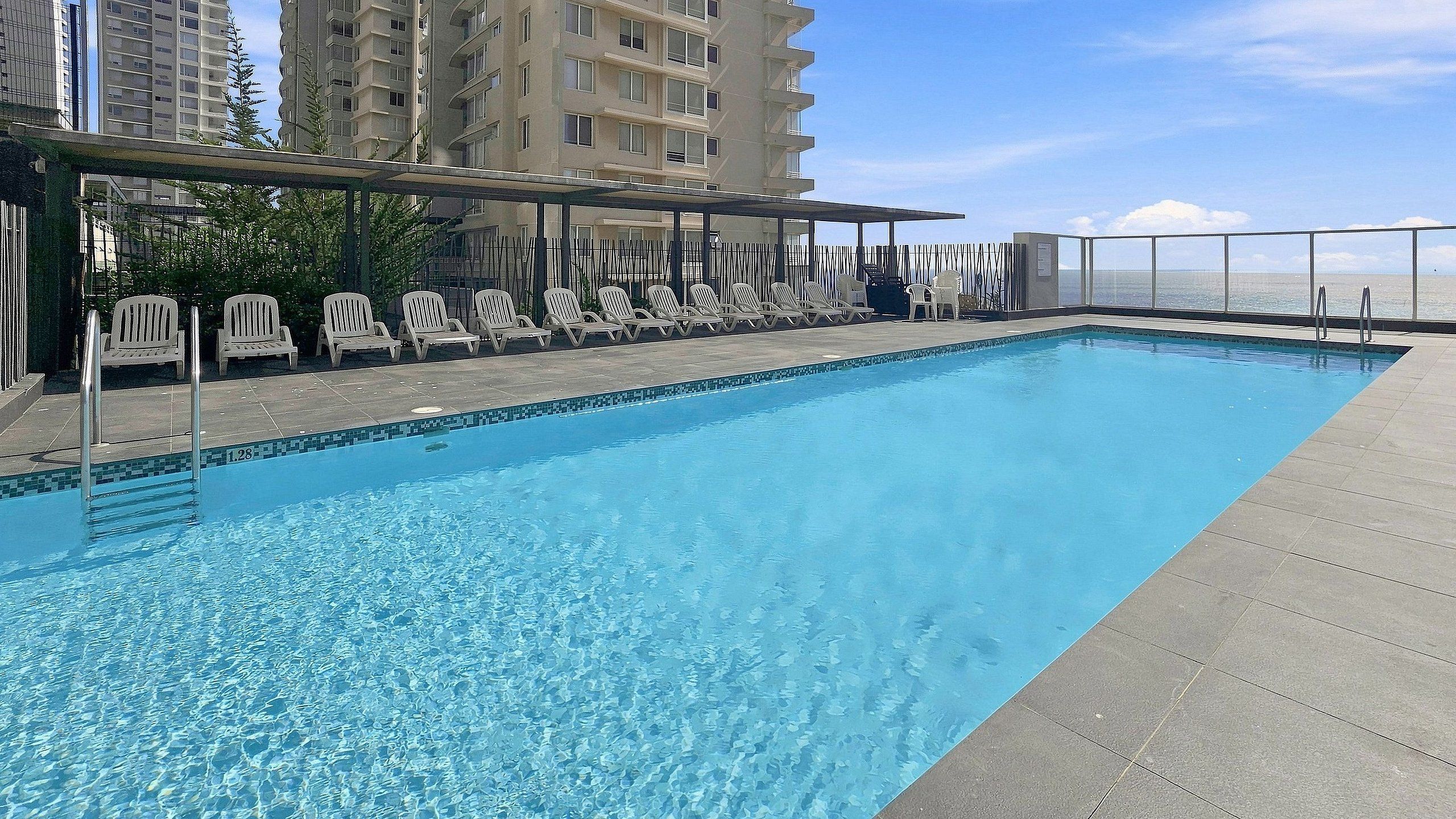 A rooftop swimming pool with lounge chairs and a view of the ocean.