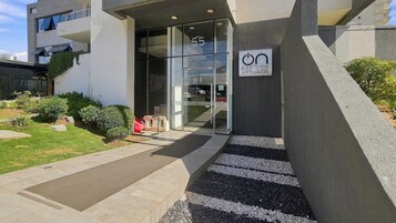 Entrada moderna de un edificio con puerta de vidrio, un letrero que dice 'Renac A Lofts & Suites' y un pequeño espacio al aire libre con un banco.