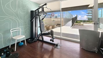 Un gimnasio con equipo de ejercicio, una silla y vistas a un edificio y al cielo.