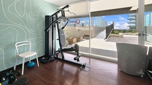 Een sportschool met trainingsapparatuur, een stoel en uitzicht op een gebouw en de lucht.