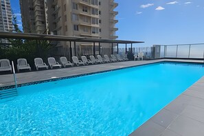 A swimming pool with lounge chairs and a covered area, surrounded by high-rise buildings.