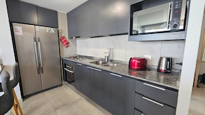 A modern kitchen with stainless steel appliances, a microwave, a red toaster, and a sink. - Oceana Suites Reñaca Norte (Vina del Mar)