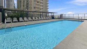 Una piscina en la azotea con sillones de descanso y vistas al océano.