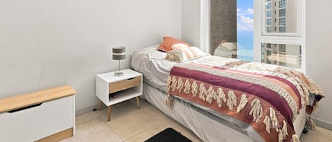 A modern bedroom with a bed, bedside table, and a window with a view of buildings.