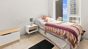 A modern bedroom with a bed, bedside table, and a window with a view of buildings. - Oceana Suites Reñaca Norte (Vina del Mar)